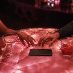 Two adults reaching toward each other across a pink cocktail table