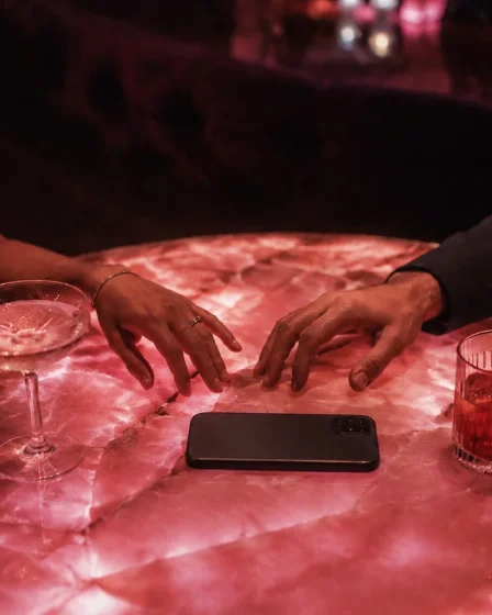 Two adults reaching toward each other across a pink cocktail table