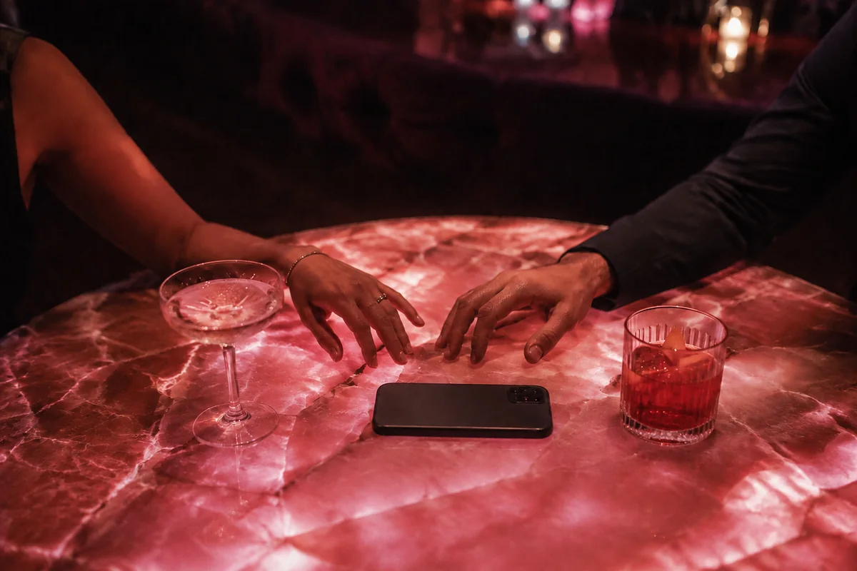 Two adults reaching toward each other across a pink cocktail table